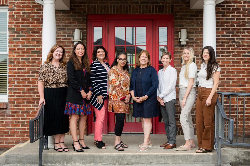 Gilda's Club staff stand on the front steps of their office building with a red door in the background.